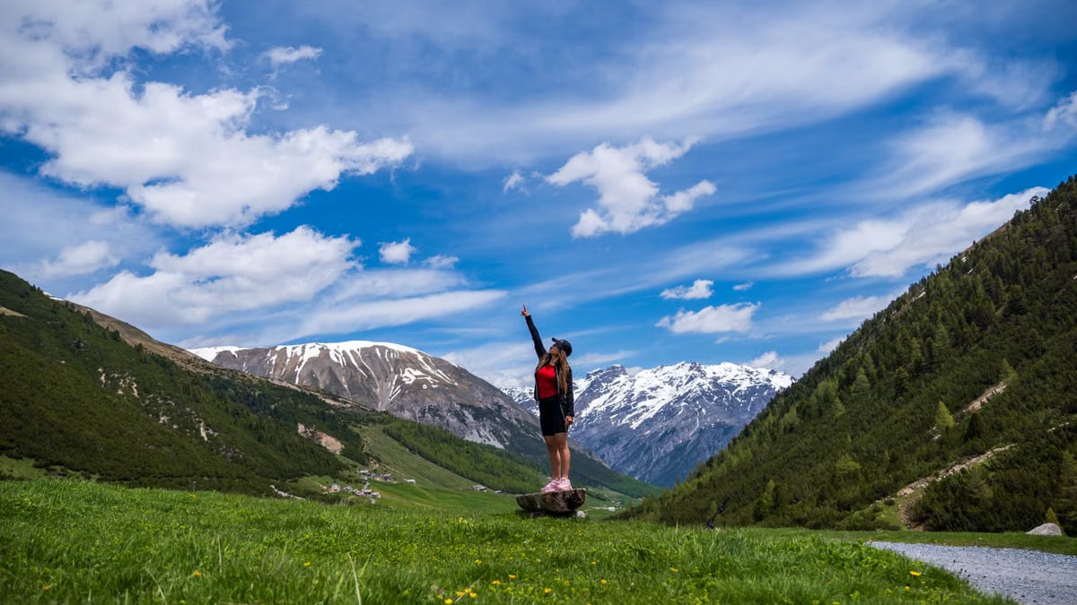 Woman celebrating atop a hill in Livigno, Italy, with stunning mountain views.